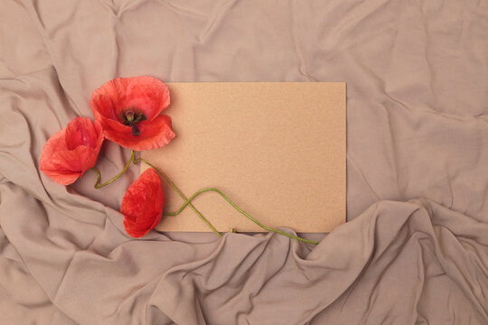Beige paper frame, red poppy flowers on crumpled wave fabric background.