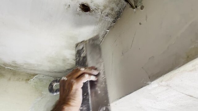 Male hand uses a putty knife to apply and spread fresh putty on interior wall. Worker carefully levels the material preparing surface for finishing and creating smooth base for further renovation work