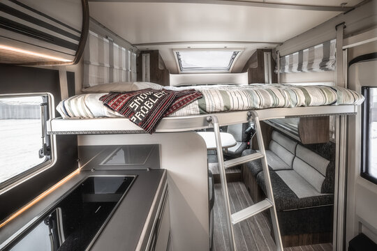 View of the modern interior of a camper van featuring a raised bed with a ladder, a small kitchen area, and a seating area, Normandy, France.