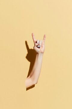 Hand making a rock gesture with a luminous glow and visible skin texture against a warm amber background with copy space for music culture