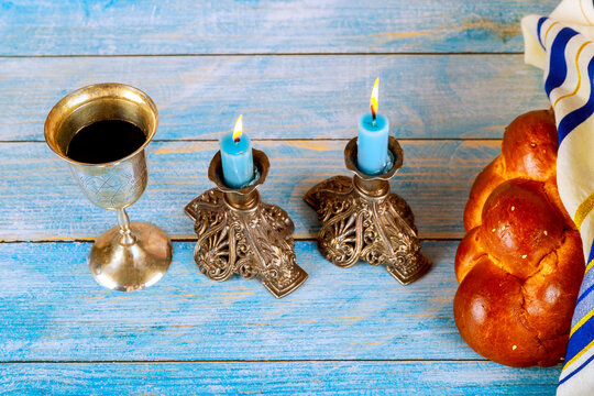 Jewish Shabbat candles wine glass with challah bread on blue wooden table