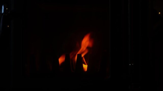 Close-up static shot of bright orange flames burning behind an iron grate in a dark fireplace