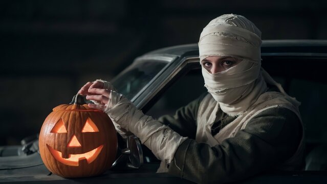Person in mummy costume with glowing jack-o-lantern pumpkin for Halloween celebration