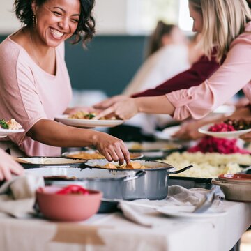 Plus size Black woman smiling by a potluck table with colorful vegetarian dishes and oil slicked stews for community and plant based events, copy space