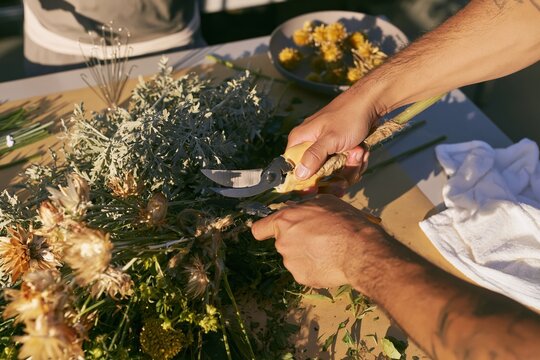 Man using secateurs to cut floral stems on a muted beige counter with, for restaurant table styling and florist work