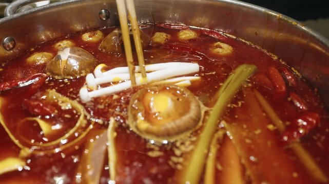 Slow Motion Close-up Chopsticks Placing Enoki Mushrooms into Spicy Hot