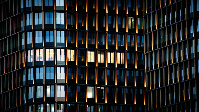 Modern glass office building facade illuminated at night. Urban architecture with reflective windows and warm lights representing business, technology, and contemporary city development.