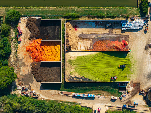 Aerial view of a composting facility with large rectangular bays containing colorful piles of organic material and machinery working on site in Pomposa, Emilia-Romagna, Italy.