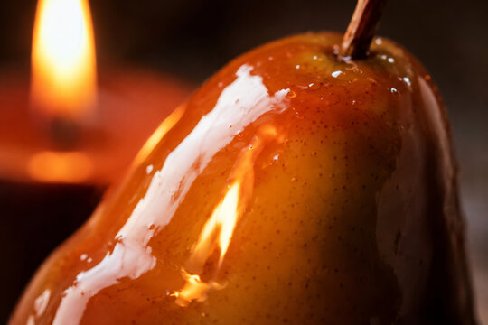 Close up of pear coated in molten caramel and heated by flame. Caramelization process in dessert preparation. Gourmet confectionery and culinary technique concept.