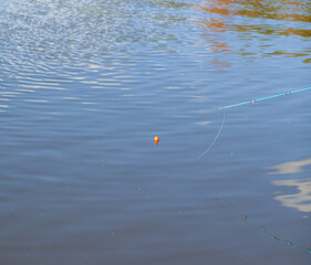 Fishing bobber is visible on the surface of a tranquil lake, surrounded by gentle ripples and reflections of the surrounding environment © Anat art