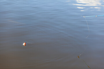 Fishing bobber is visible on the surface of still water, with fishing line trailing beneath it into the depths of the water body © Anat art