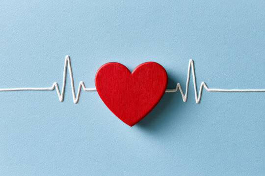 Red wooden heart connects to a white heartbeat line on a blue background. Heart health, cardiac care, medical awareness.