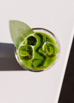 Close up of iced green matcha tea. Creative trendy healthy drink background concept. Matcha texture backdrop idea with ice, matcha bumble with orange juice. Flat lay style. Top view banner