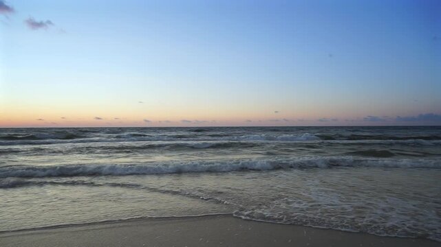 Baltic Sea seascape at twilight a few minutes after sunset, with rough waves rolling toward a sandy beach under a calm summer sky and colorful evening light.