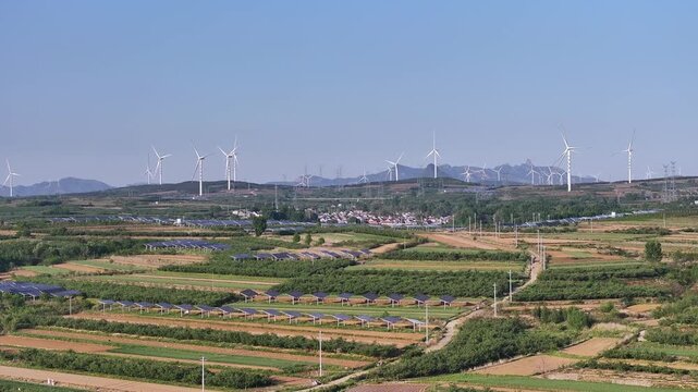 Hilly farmland landscape featuring wind turbines and solar panels under clear blue sky