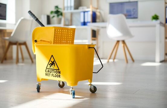 Cleaning bucket mop in office hygiene safety. Bright yellow wet floor bucket with wringer, caution sign in an office, signaling maintenance and spill prevention. Clean and safe office concept.