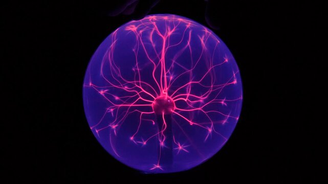Boule plasma interactive avec une main touchant la surface, g&eacute;n&eacute;rant des filaments lumineux color&eacute;s. Exp&eacute;rience scientifique et effet &eacute;lectromagn&eacute;tique fascinant sur fond sombre.