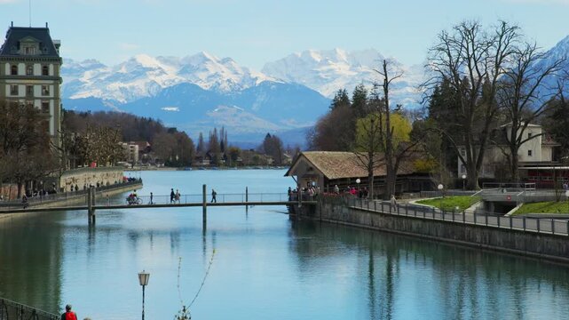 Static view of pedestrians on bridge in Thun with snow capped Alps background