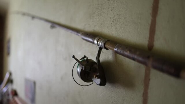 Vintage fishing rod and reel hang on an old wall showing classic angling gear with worn details rustic character and nostalgic outdoor sporting heritage inside old storage