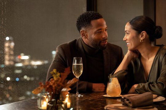 African american man and woman on romantic dinner date at city restaurant window. Couple drinking non alcoholic cocktail and champagne. Night time autumn celebration and lifestyle.