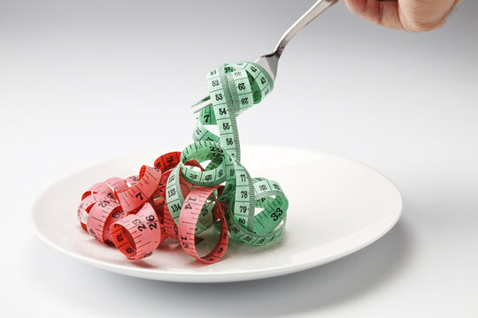 Measuring tape shaped like spaghetti pasta on a fork over a white plate representing diet concept