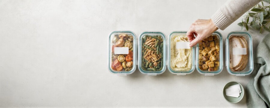 Woman labeling glass containers with leftover Thanksgiving food. Sustainable meal prep with healthy holiday dinner dishes in zero waste storage boxes.