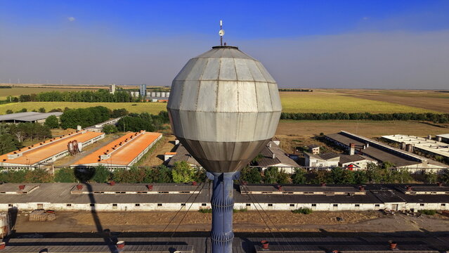 Aerial view of a spherical metal water tower situated on a farm with agricultural buildings and fields in the background in Dolovo, Vojvodina, Serbia.