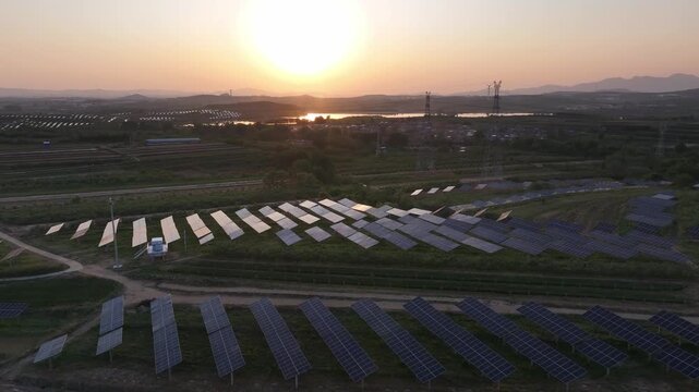 Solar power station in rural fields during sunset with orderly panel arrays and distant hills
