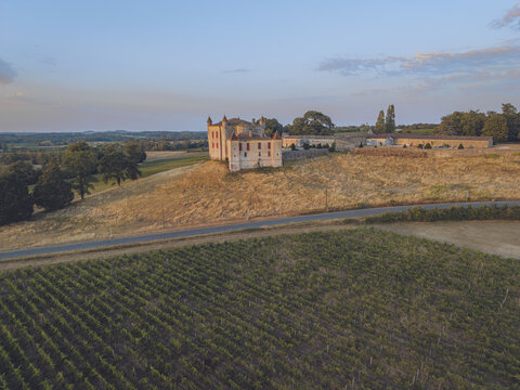 Aerial view of a historic chateau surrounded by lush vineyards and rolling hills during the golden hour in Puisseguin, Nouvelle-Aquitaine, France.