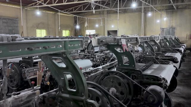 Interior view of a textile weaving factory multiple rows of mechanical power looms producing white fabric,