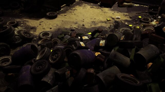Dark pile of discarded tires under dim yellow light, muddy ground scattered with rims and leaves, oil stains and gritty textures, atmosphere of neglect