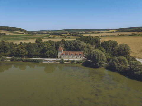 Aerial view of the historic stone building at etang du patis surrounded by lush trees and agricultural fields in Bligny, Grand Est, France.