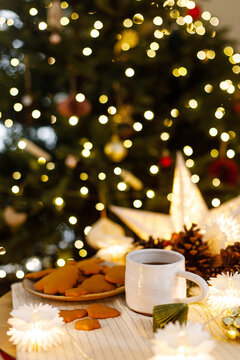 Cozy winter scene with mug of hot tea, gingerbread cookies, and Christmas tree lights bokeh. Merry Christmas. Hygge winter holidays