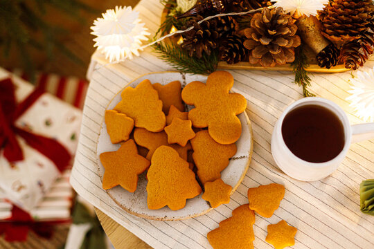 Homemade Christmas Gingerbread Cookies with Cup of Tea and Pine Cones on Table with Garland Lights, top view. Cozy Christmas eve, winter holidays