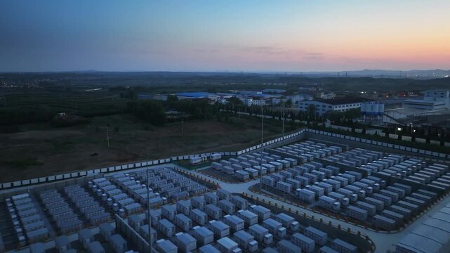 Aerial view of a large-scale energy storage station at dusk with neatly arranged battery modules and industrial facilities