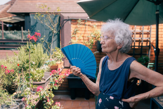 old woman cooling herself with a fan while sitting on the balcony during a heatwave