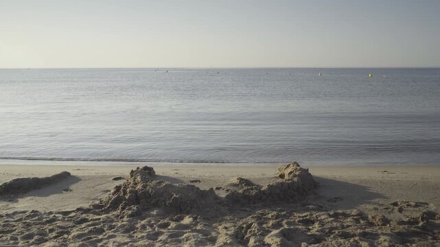 France, Valras Plage August 08, 2026 &mdash; Handheld shot of a sand castle built on an empty beach with calm Mediterranean sea water and a clear horizon during a peaceful sunny morning
