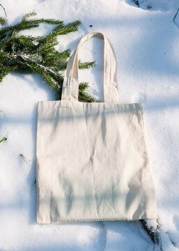 White cotton mesh bag on winter snow with fir tree branches background. Zero waste, no plastic, eco friendly shopping, recycling, christmas concept. Blank mockup, place for text. copy space flat lay