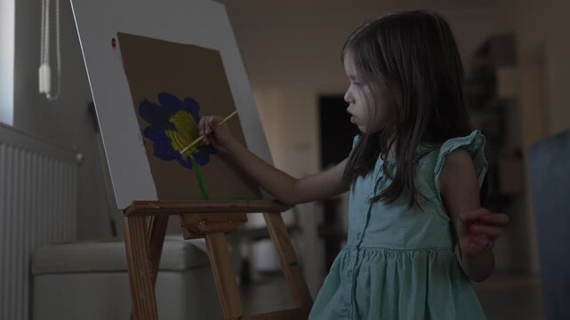 Talented little girl painting flower on easel