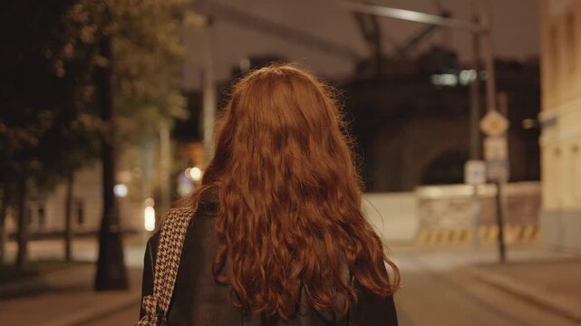 Cinematic girl with long wavy red hair in a black leather jacket, standing on a night city street and watching a train, dreaming of a journey.