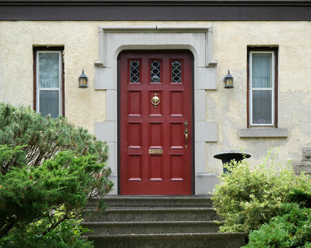 Front door and front steps of old stucco house, surrounded by shrubbery