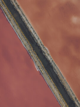 Aerial view of the vibrant pink salt pans at Salin d'Aigues-Mortes, featuring a narrow dark water channel dividing the colorful basins in Aigues-Mortes, Occitanie, France.