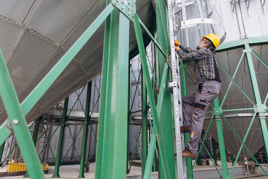 Farm worker climbing a grain silo ladder, inspecting the granary elevator structure and agriculture industry equipment