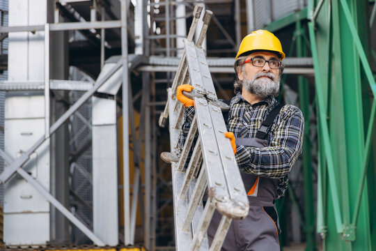 Senior worker carrying a ladder, preparing for maintenance work at a grain elevator facility