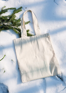 White cotton mesh bag on winter snow with fir tree branches background. Zero waste, no plastic, eco friendly shopping, recycling, christmas concept. Blank mockup, place for text. copy space flat lay