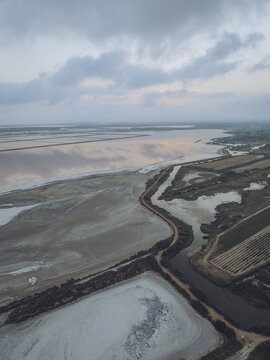 Aerial view of Salin d'Aigues-Mortes featuring expansive salt pans with reflective water surfaces under a cloudy sky in Aigues-Mortes, Occitanie, France.