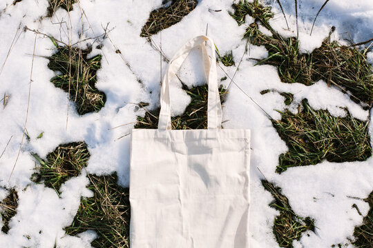 White cotton mesh bag on spring snow, green grass thawed patches background. Zero waste, no plastic, eco friendly shopping, recycling concept. Blank mockup shopper, place for text. copy space flat lay