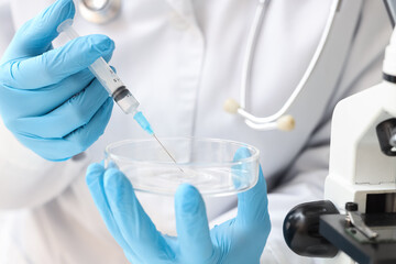 Fototapeta premium Scientist in blue gloves holding a syringe and petri dish, medical research and laboratory experiment concept, a stethoscope and microscope are visible in the background