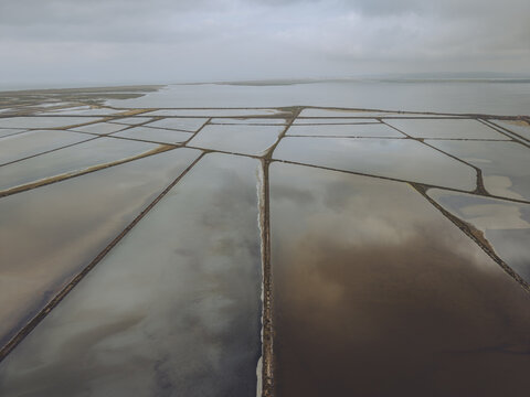 Aerial view of Le Salin de l'ile Saint-Martin de Gruissan featuring geometric salt evaporation ponds with varying water colors under a cloudy sky in Gruissan, Occitanie, France.