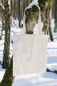 White cotton mesh bag hanging on tree branch, winter forest, sunny day background. Zero waste, no plastic, eco friendly shopping, recycling, christmas concept. Blank mockup, place for text copy space